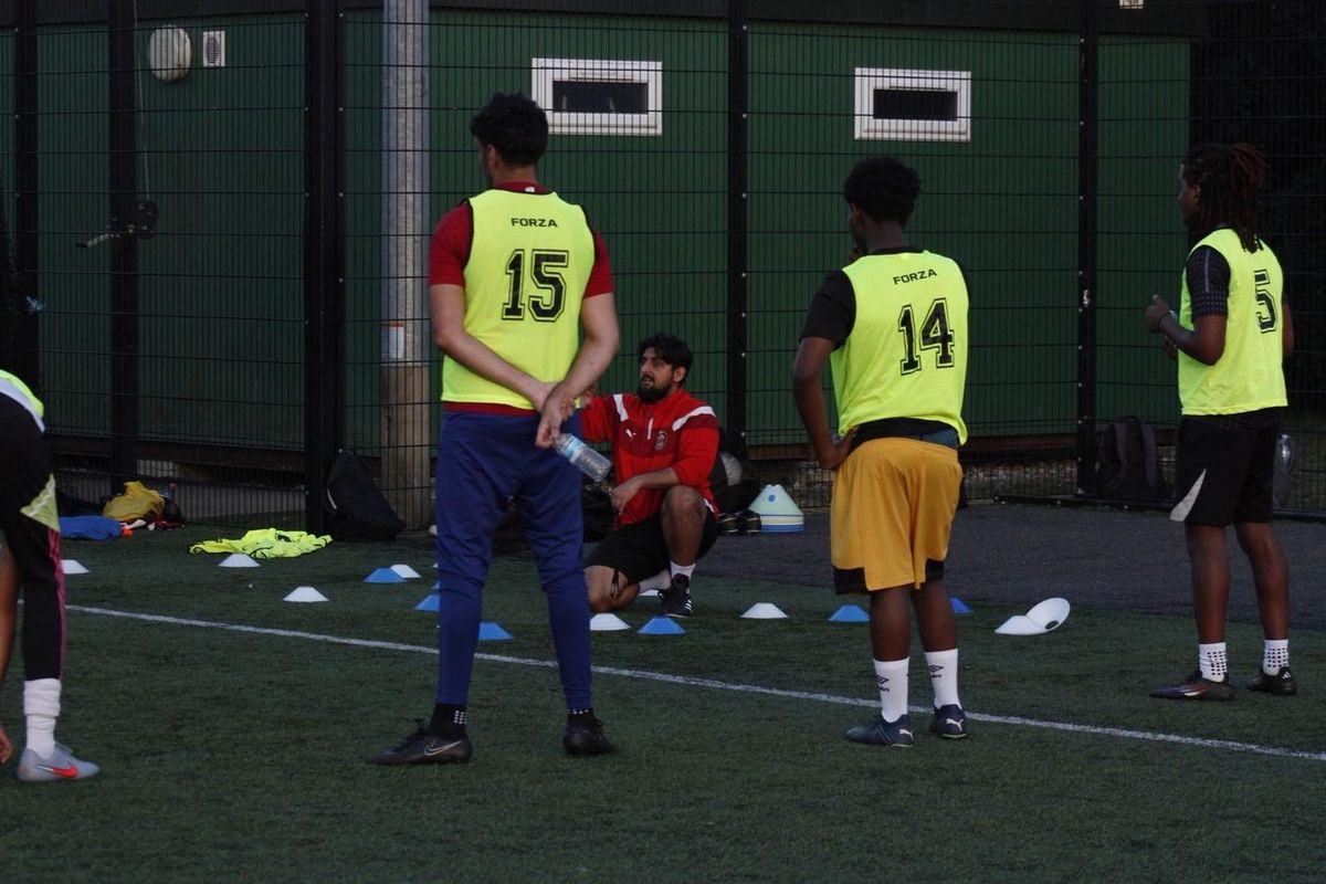 Coach T talking to a group of players during a training session on a floodlit pitch