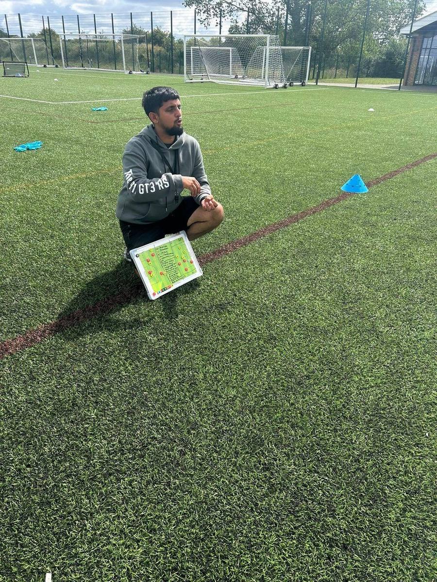 Coach T kneeling on the pitch with a tactics board during a session